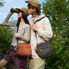 A young couple outdoors wearing casual clothing and carrying a water resistant crossbody shoulder bag.