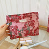 A pink cosmetic pouch with a floral pattern is held against a white paneled background.