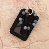Black leather card holder with a gold keychain and a bracelet of gray and black beads