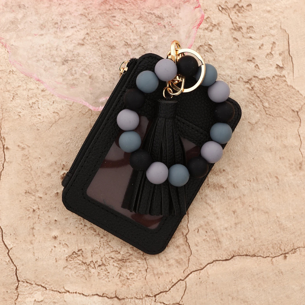 Black leather card holder with a gold keychain and a bracelet of gray and black beads
