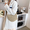 A woman wearing a white coat and light skirt holds a handmade rattan straw crossbody bag.