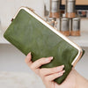 Eine Hand hält eine dunkel olivgrüne Vintage-Clutch-Geldbörse mit goldenen Verzierungen.