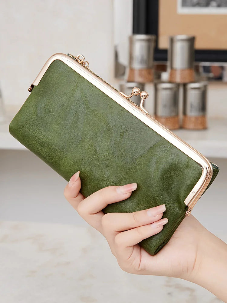 Eine Hand hält eine dunkel olivgrüne Vintage-Clutch-Geldbörse mit goldenen Verzierungen.