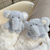 A soft gray plush elephant case for AirPods resting on a white fluffy surface.