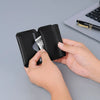 A hand holds a black magnetic foldable ID card holder and coin purse next to a silver card on a gray surface.