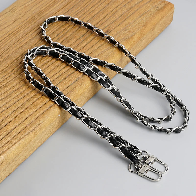 A silver and black leather chain strap is displayed on a wooden surface.