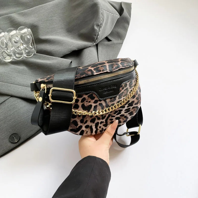 Eine Hand hält eine schwarz-leopardmusterige Crossbody-Bauchtasche mit goldfarbenen Verzierungen vor einem grauen Sakkojacke.