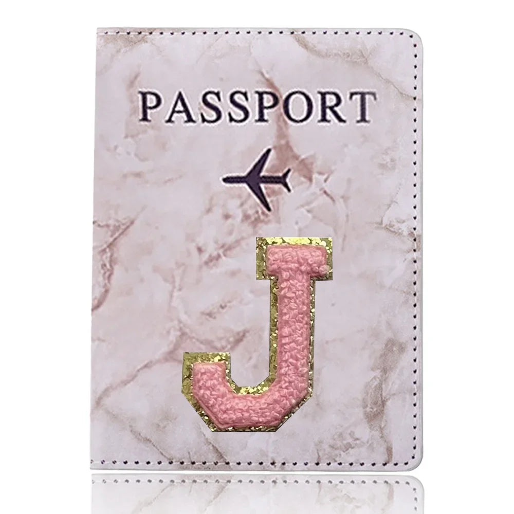 Portafolio de pasaporte de cuero marmolado rosa con una J dorada grabada en la parte delantera.