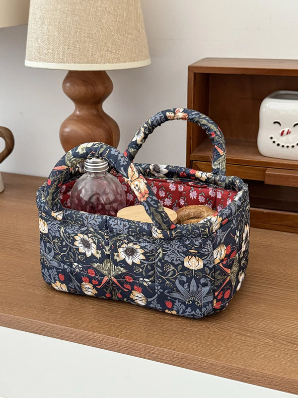 A dark floral quilted fabric storage basket holding a glass bottle, resting on a wooden surface.