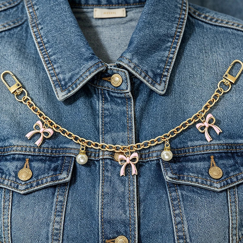 A denim jacket adorned with a gold chain necklace featuring pink bows and pearl charms.