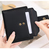 A black RFID blocking bi-fold card holder wallet is shown being held by a hand, displaying the interior and gold-colored snap