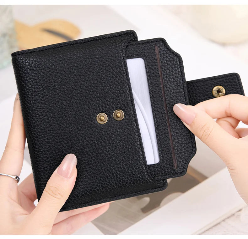 A black RFID blocking bi-fold card holder wallet is shown being held by a hand, displaying the interior and gold-colored snap