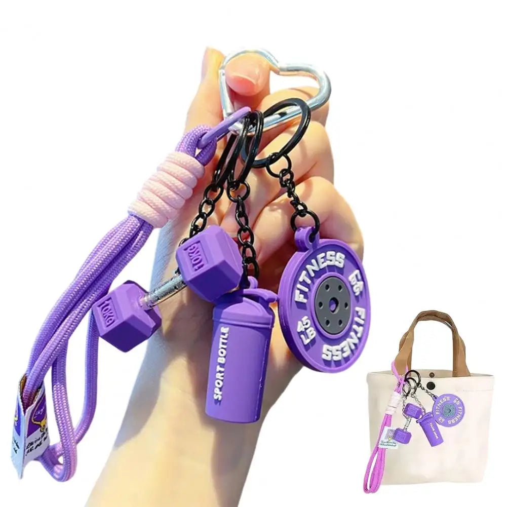 A hand holds a purple fitness keychain featuring a dumbbell and kettlebell charm.