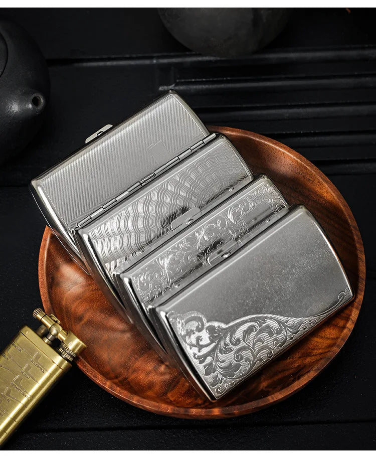 A silver metal cigarette case is shown open, resting on a wooden tray next to a gold-colored lighter.
