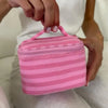 A hand holds a pink striped Y2K makeup bag with a zipper on a person's white shirt.