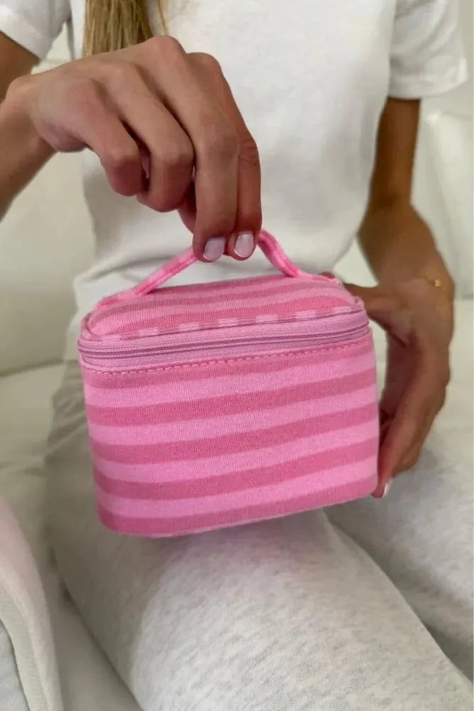 A hand holds a pink striped Y2K makeup bag with a zipper on a person's white shirt.
