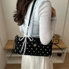 Eine Frau hält eine schwarze Schultertasche mit weißen Polka Dots vor einem hellen Hintergrund.