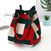 A deep green and red plaid knit bucket tote bag with leather handles resting on a white surface.