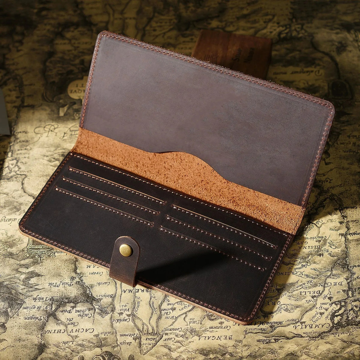 A brown genuine leather long bi-fold wallet with a snap closure resting on aged paper.