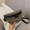 Sac bandoulière à motif léopard noir et or posé sur un tissu tricoté blanc, sur un canapé gris.