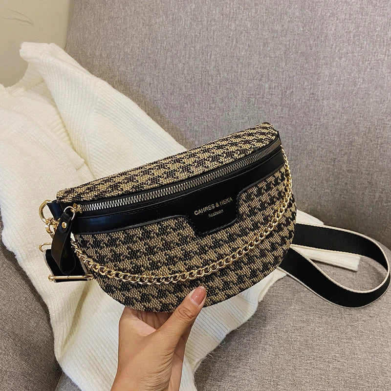 Sac bandoulière à motif léopard noir et or posé sur un tissu tricoté blanc, sur un canapé gris.