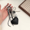 A black leather heart key chain with silver charms and a black and white patterned charm is held in a hand.