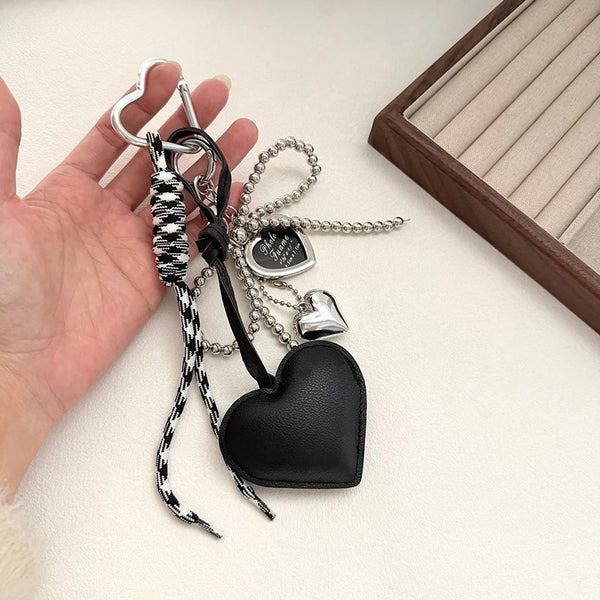 Eine schwarze Lederherz-Anhänger mit silbernen Anhängern und einem schwarz-weißen Muster wird in einer Hand gehalten.