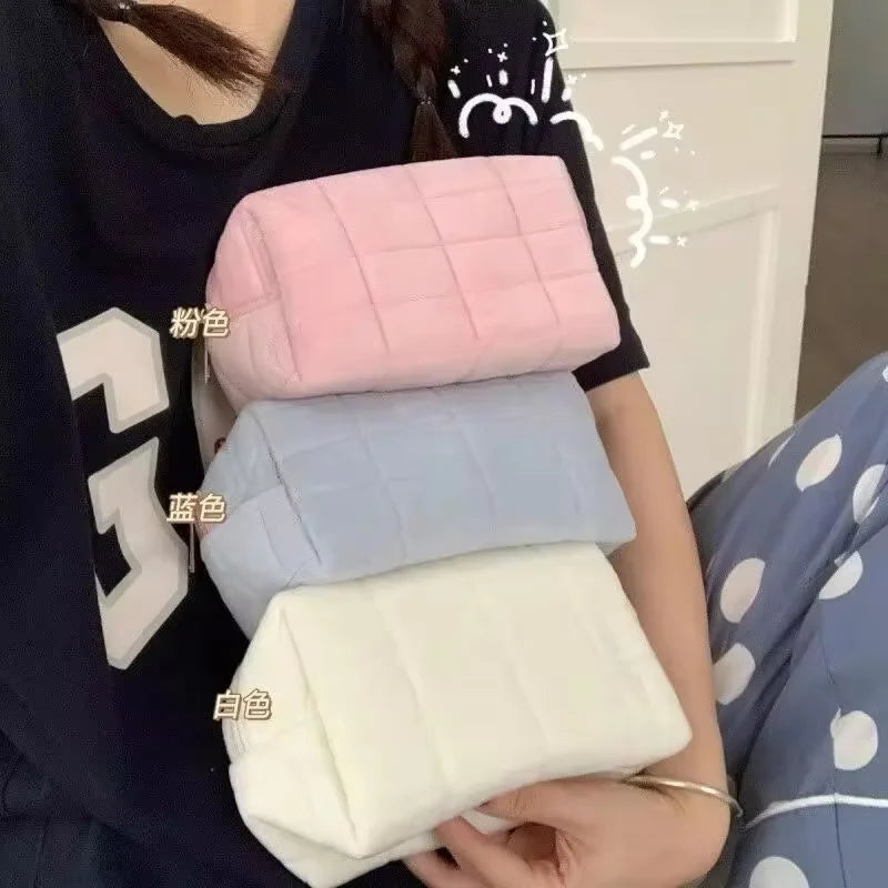 A hand holds a stack of quilted cosmetic storage pouches in pink, blue, and white colors.