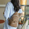 Eine Person hält eine braune Kunstleder-Crossbody-Tasche mit einem goldfarbenen verstellbaren Riemen.