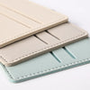 Tres porta tarjetas de cuero PU apilados en colores beige, gris claro y verde menta.