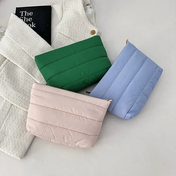 Three quilted cosmetic travel bags in shades of green, blue, and pink are displayed on a white surface.
