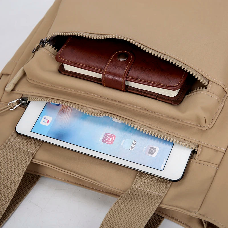 A tan canvas tote bag shows a brown leather wallet and a smartphone inside the zippered compartment.
