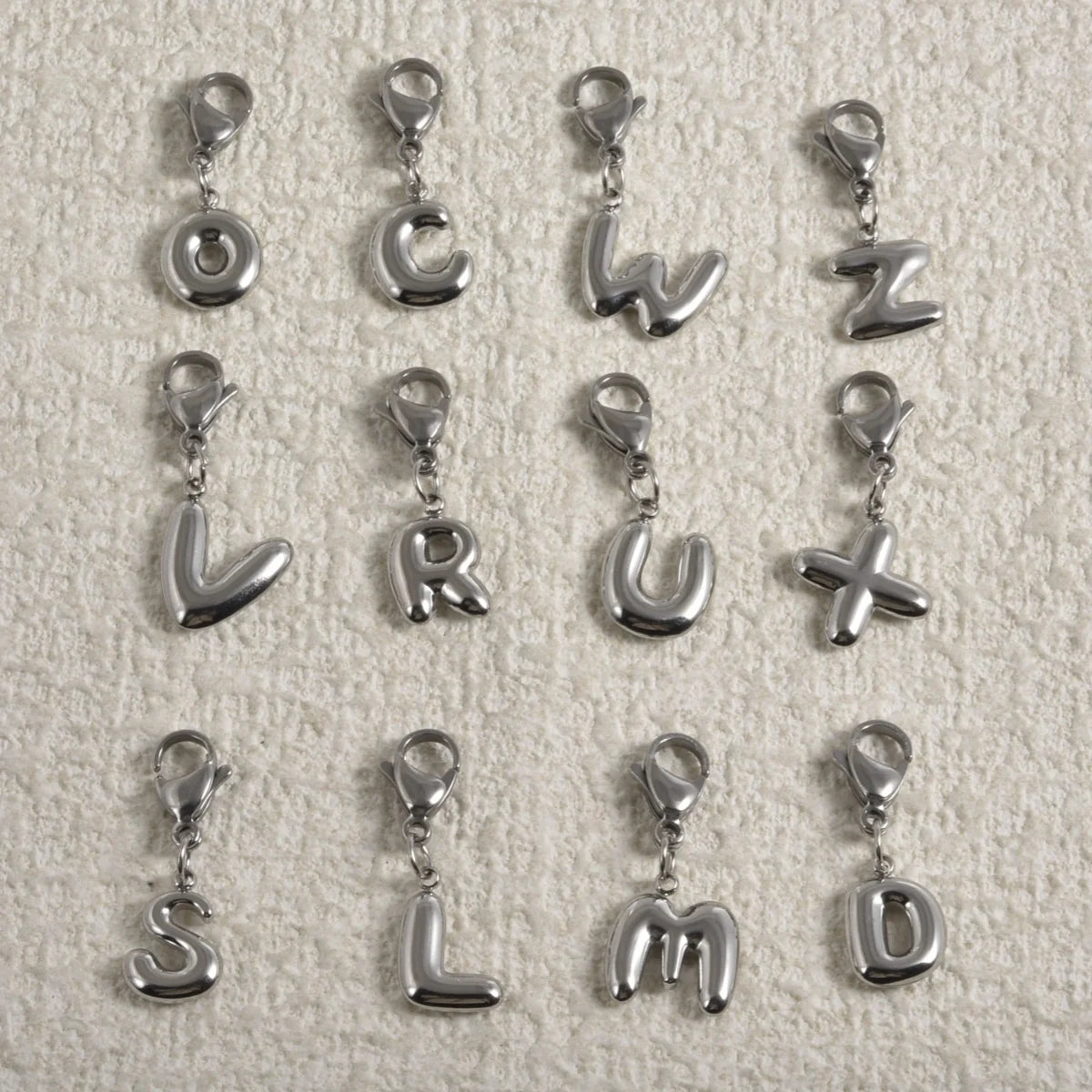 A collection of stainless steel alphabet letter charms, including O, C, W, Z, L, R, U, X, S, L, M, and D, with lobster clasps