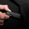 Une main tient un porte-clés organisateur de clé métallique noir minimaliste sur un fond de tissu sombre.