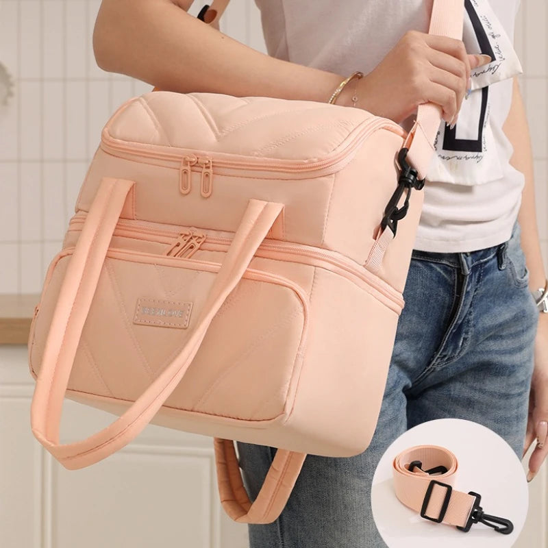 A light pink double-layer insulated lunch bag with tan straps being held by a person.