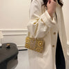 A woman wearing a cream-colored coat is holding a gold rhinestone evening clutch bag.