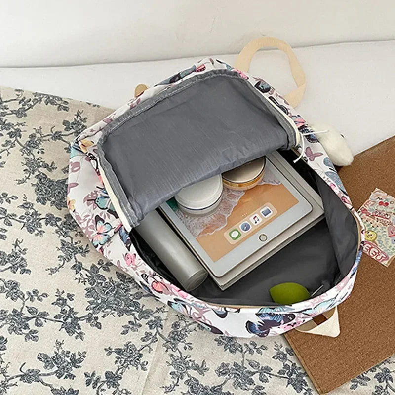 A light-colored backpack with a butterfly pattern is open, showing a laptop and storage compartments.