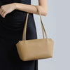 A woman holds a tan leather mini shoulder bag with adjustable straps against a light gray background.
