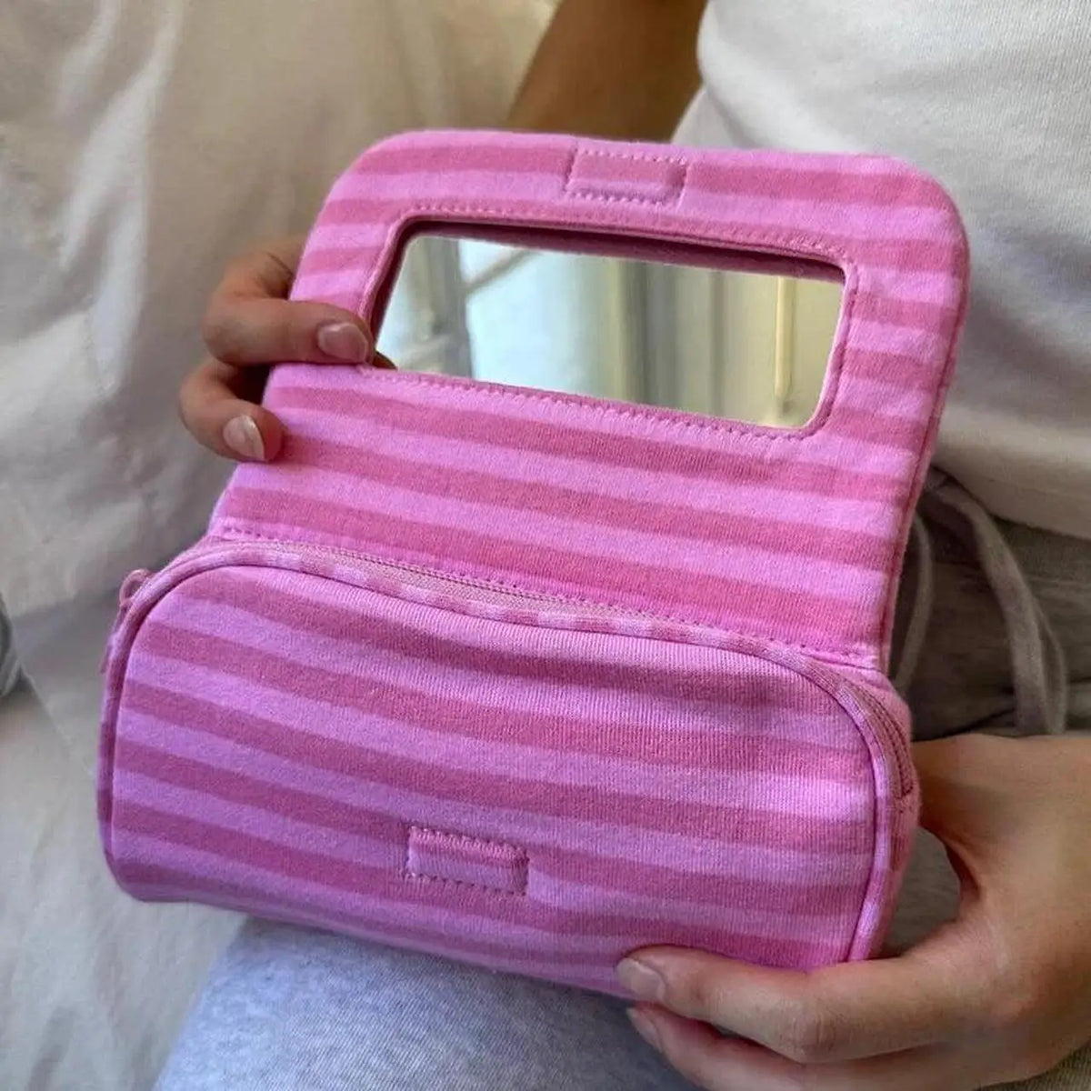 A pink striped makeup bag with a flip-top mirror being held by a person.