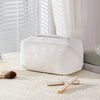 A white vintage floral waterproof makeup tote bag resting on a light surface next to a cosmetic brush and a white applicator.