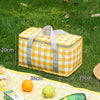 A yellow and white checkered insulated picnic tote bag lying on green grass with citrus fruits.