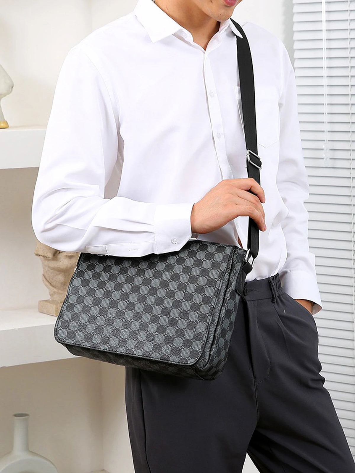 A man wearing a white shirt holds a gray plaid crossbody shoulder bag with black strap.