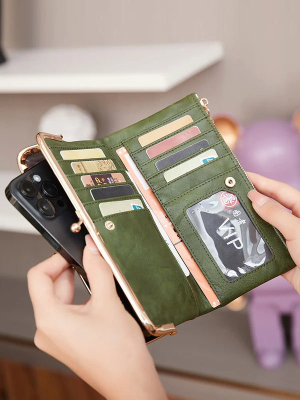 A hand holds an open olive green clutch wallet displaying various cards and cash inside.