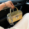 A hand holds a gold woven leather crossbody bag with silver chain straps inside a car interior.