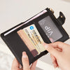 A hand is opening a black PU leather bifold wallet with an ID window, showing several credit cards inside.