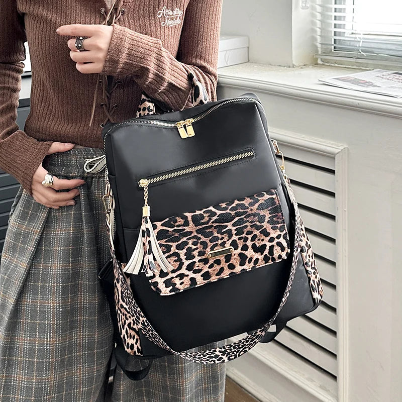 A black leopard print fashion backpack is displayed next to a person wearing a brown sweater and plaid skirt.