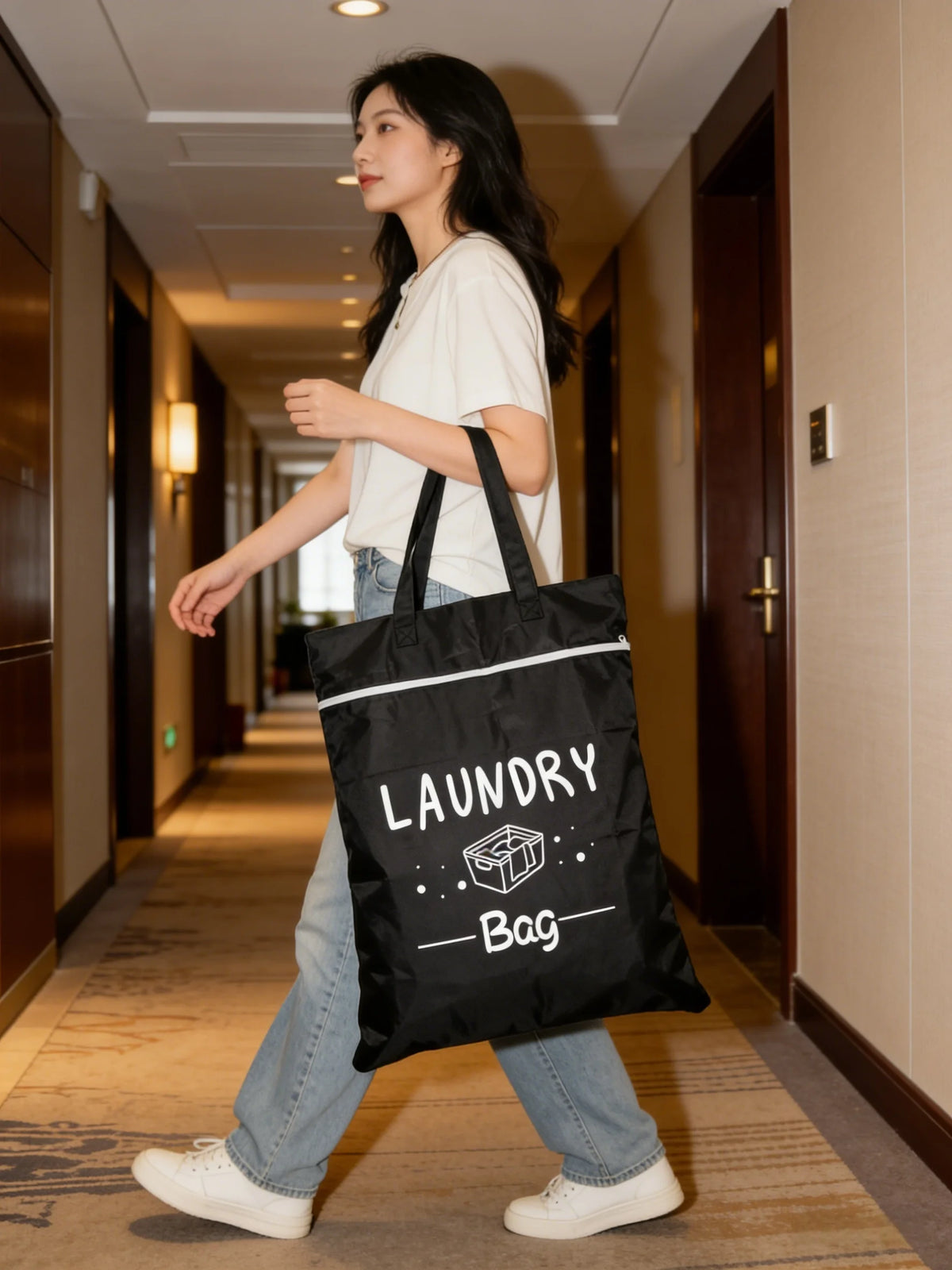 A woman walks down a hallway carrying a black laundry bag.