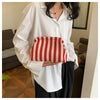 A woman holds a red and white striped crochet handbag against a white shirt.