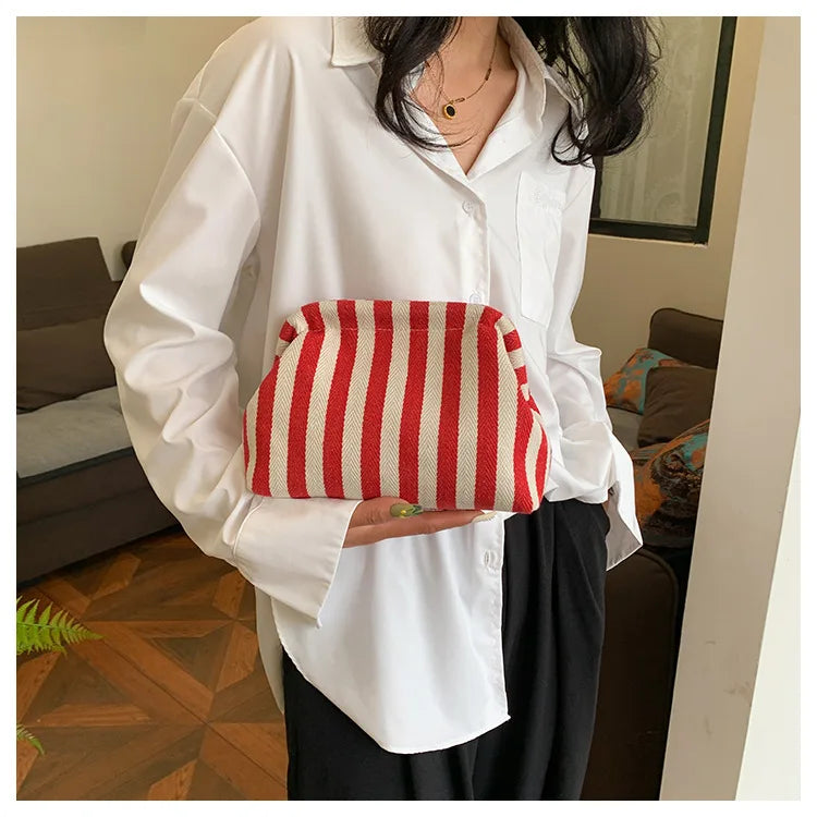 A woman holds a red and white striped crochet handbag against a white shirt.