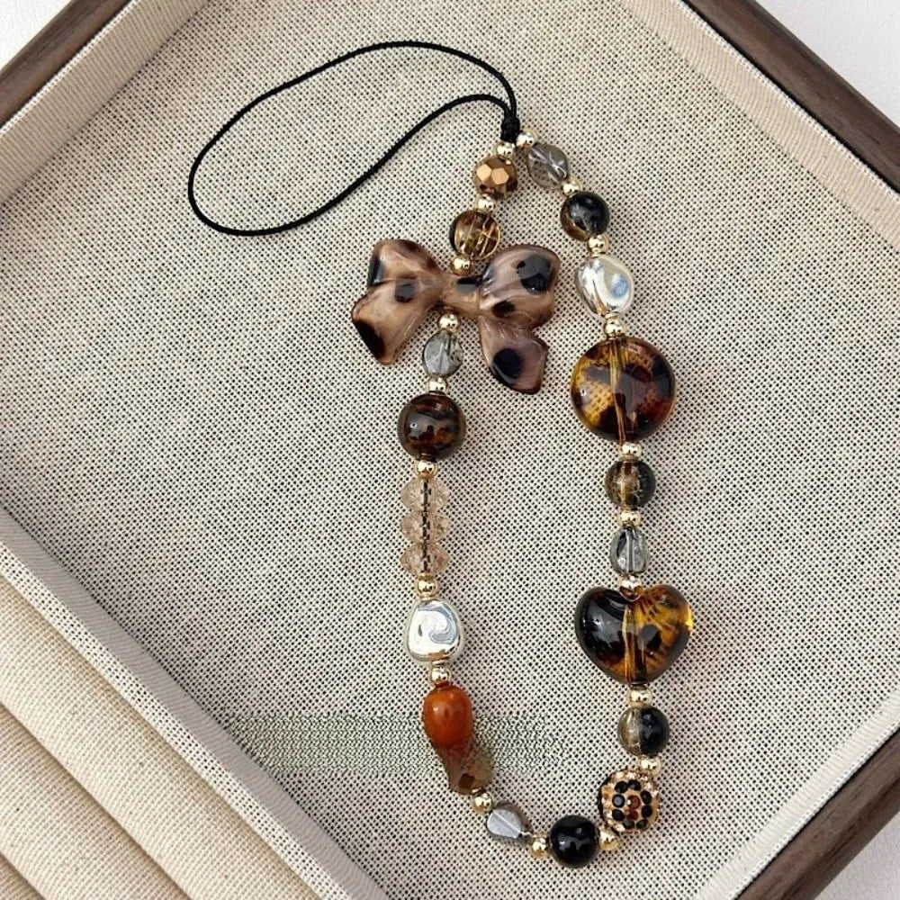 A leopard print bowknot phone lanyard featuring various heart-shaped beads and a black cord.